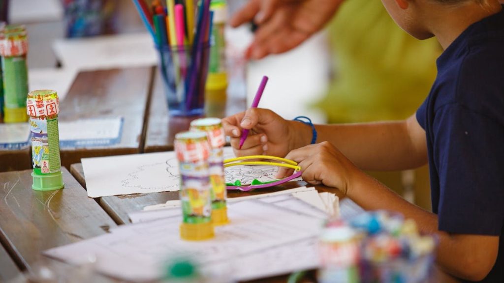 A young child focused on a drawing activity at a colorful art table indoors.